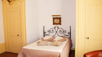 A bedroom with a bed, a chandelier, a framed picture, and two doors.