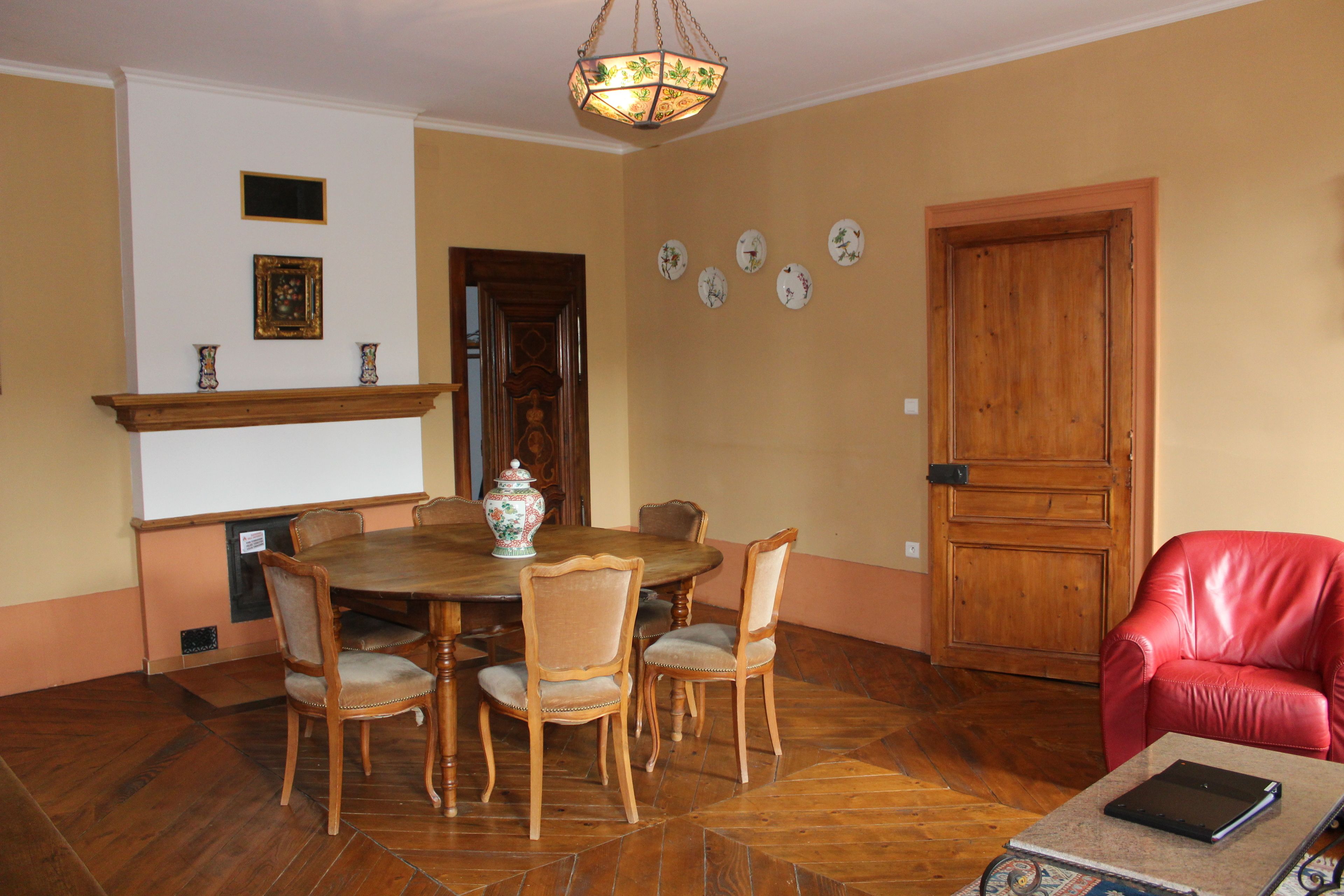 A dining room with a wooden table and chairs, a red leather chair, a wooden door, and a chandelier.