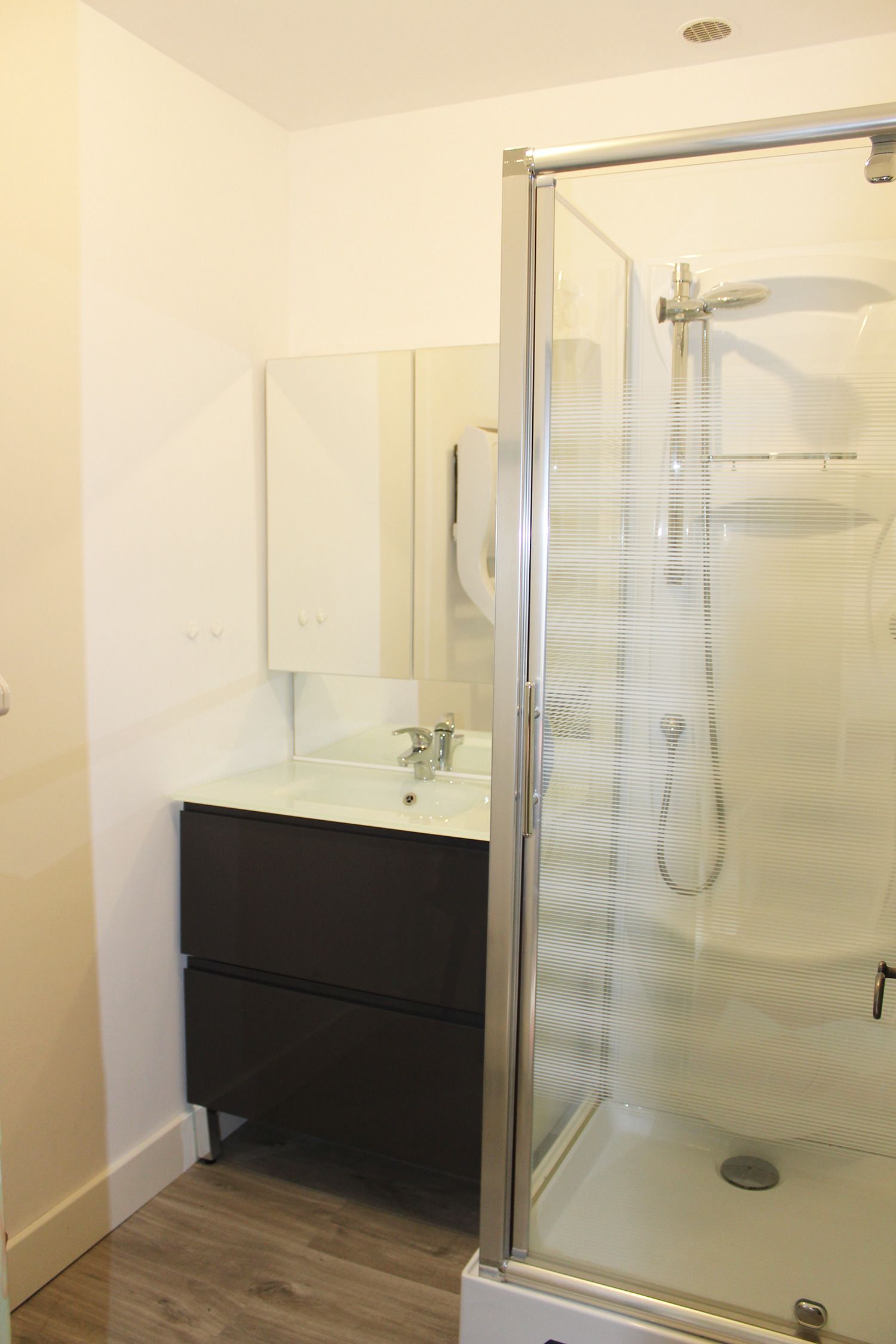 A bathroom with a glass-enclosed shower, a white sink, and a mirror above the sink.