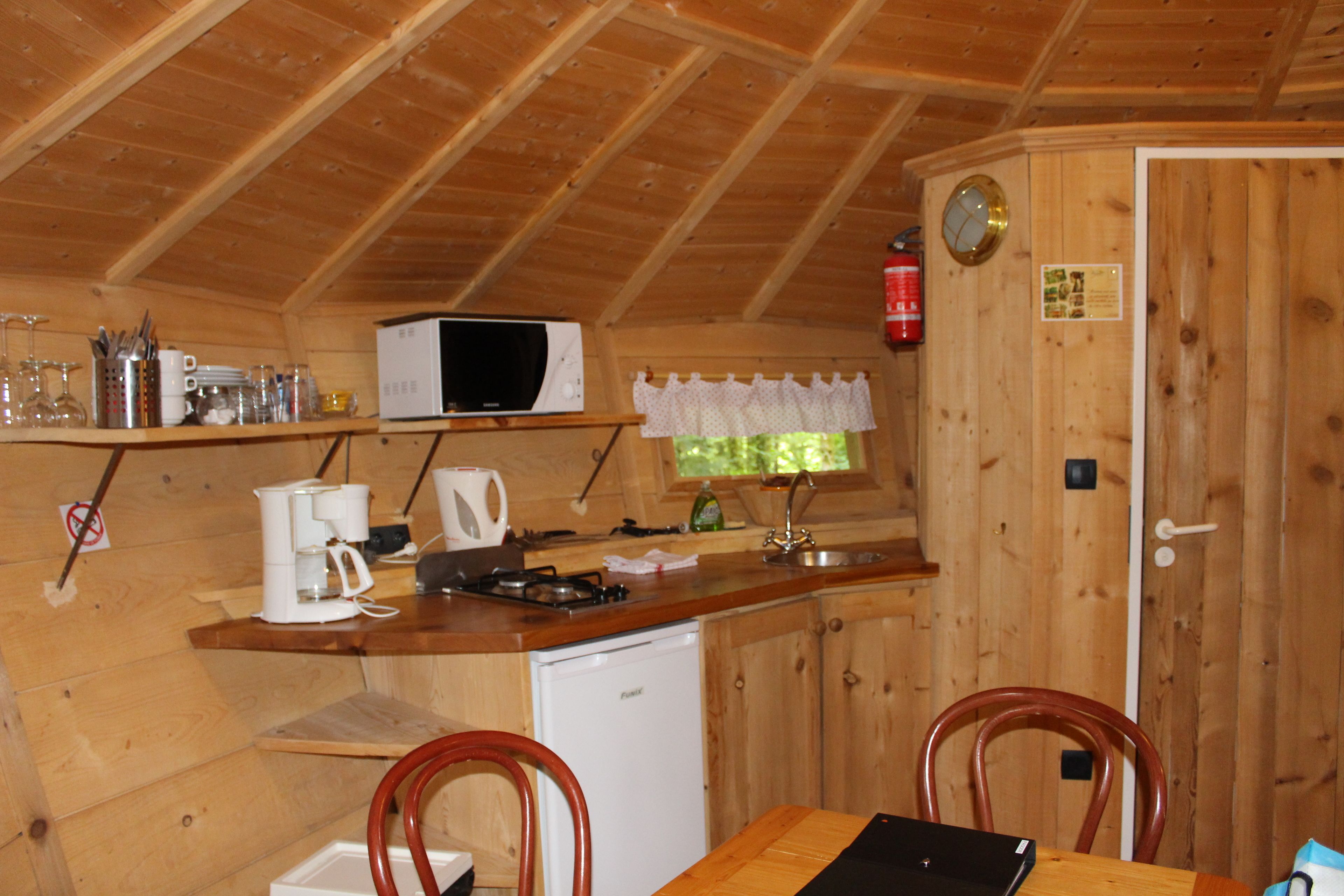 A compact kitchen with wooden walls, a microwave, a sink, and a refrigerator.
