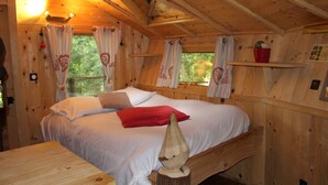 A wooden cabin bedroom with a bed, pillows, a red blanket, and a wooden headboard.