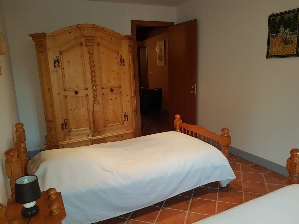 A bedroom with two single beds, a wooden wardrobe, and a nightstand with a lamp.