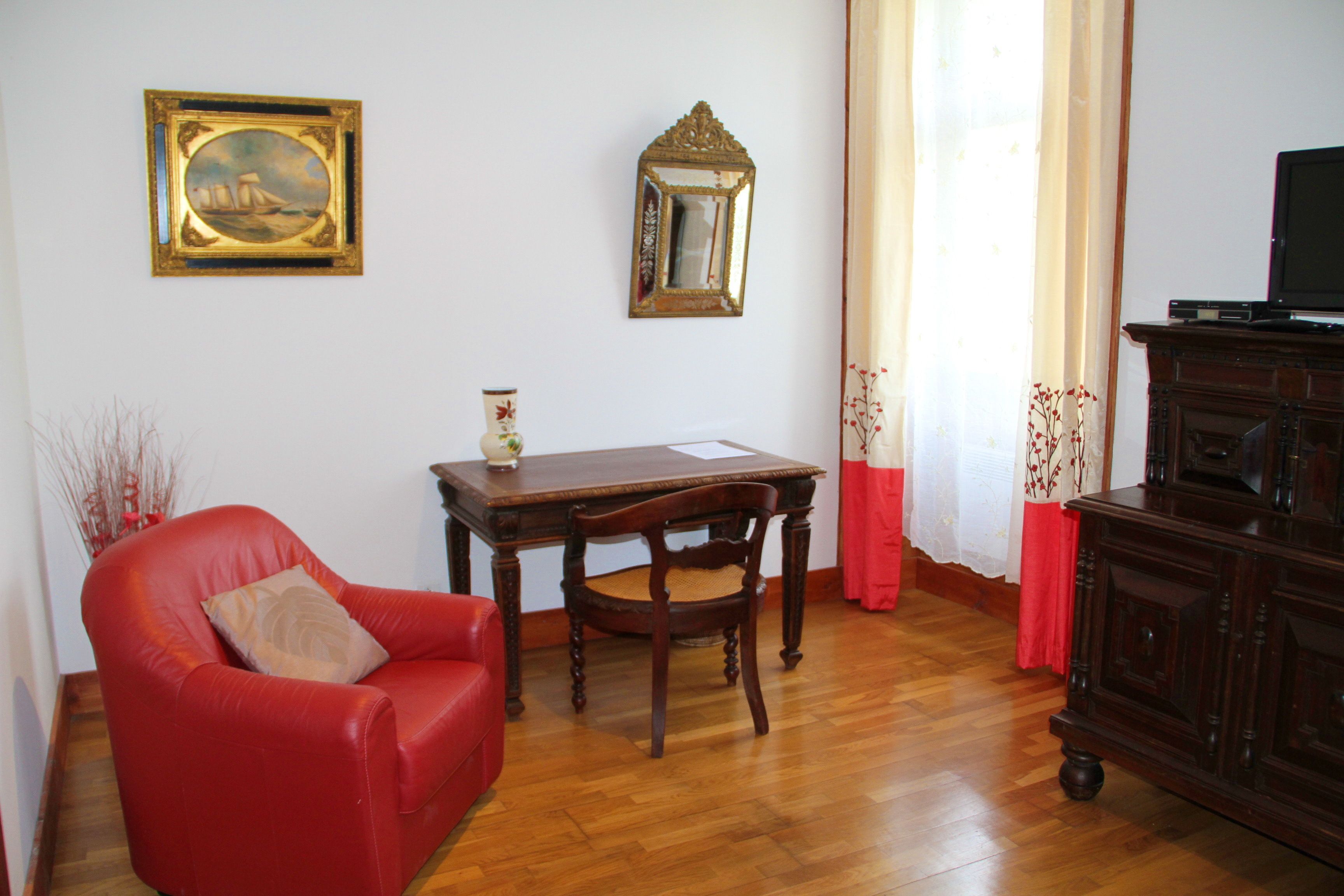 A room with a red leather chair, a wooden table, a mirror, and a television on a wooden cabinet.