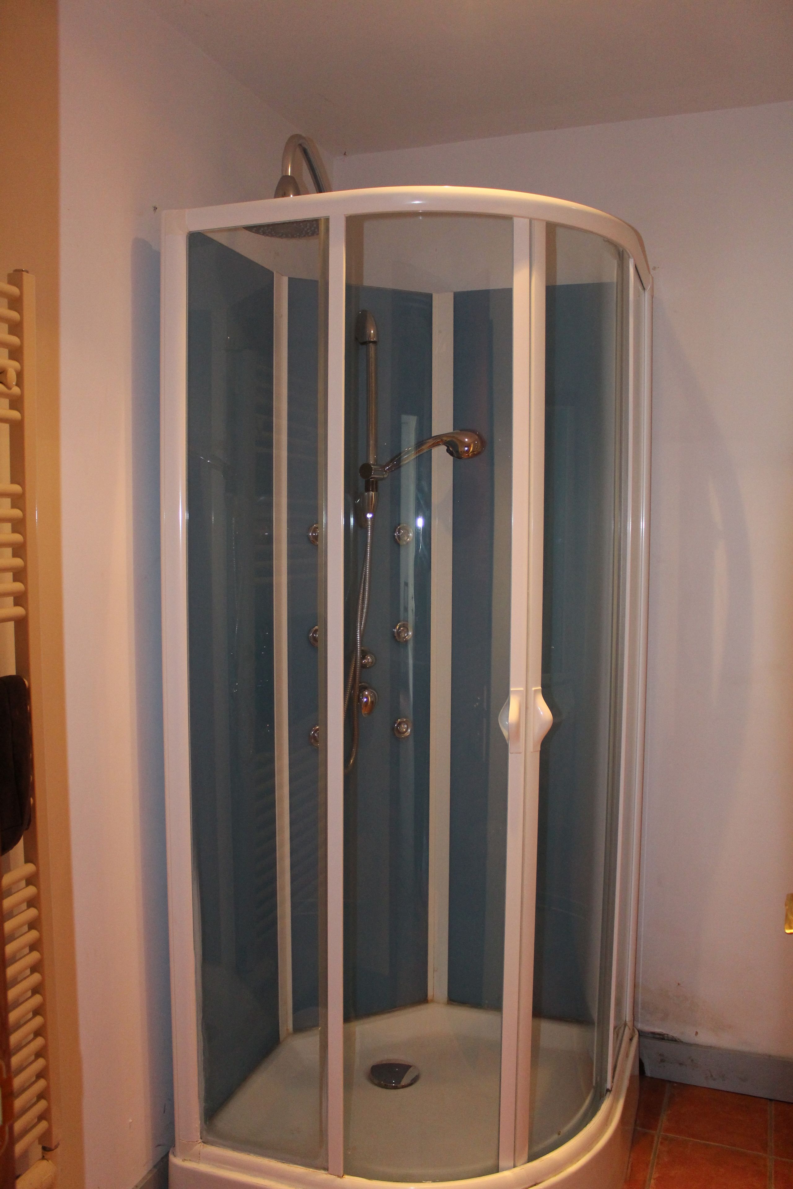 Une douche fermée par des parois en verre, avec un cadre blanc, une douchette à main et un drain situé au centre.
