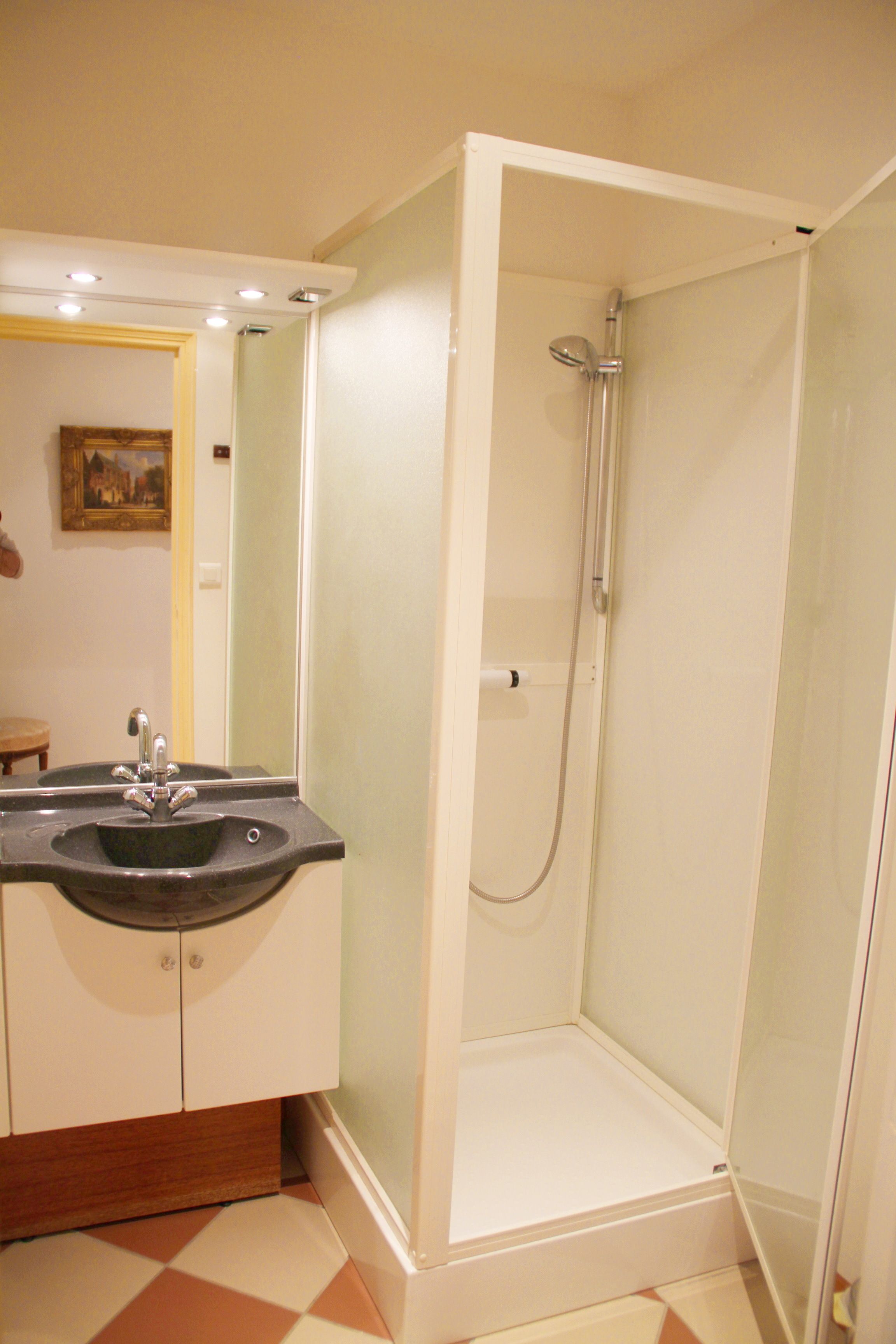 Een badkamer met een douchecabine van glas, een wastafel met spiegel en een zwart-witte vloer.