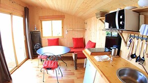 A compact kitchen with wooden cabinetry, a round table, red chairs, and a window providing natural light.