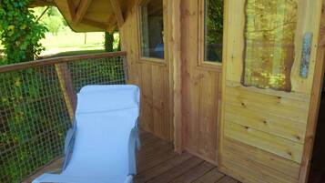 Una cabaña de madera con un porche cubierto, una silla de descanso blanca y una ventana con vistas a la vegetación.