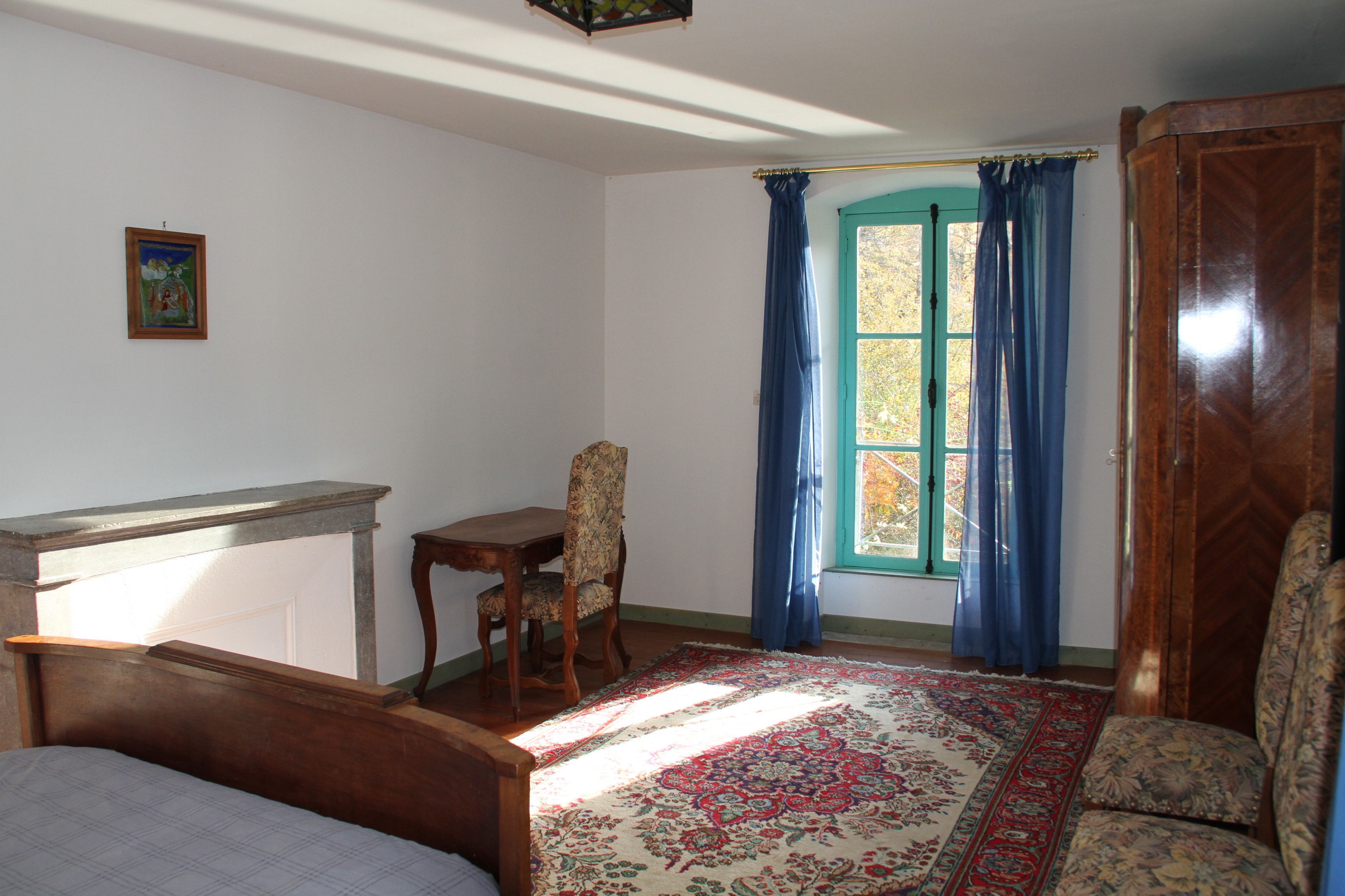A room with a bed, a desk, a chair, and a window with curtains.