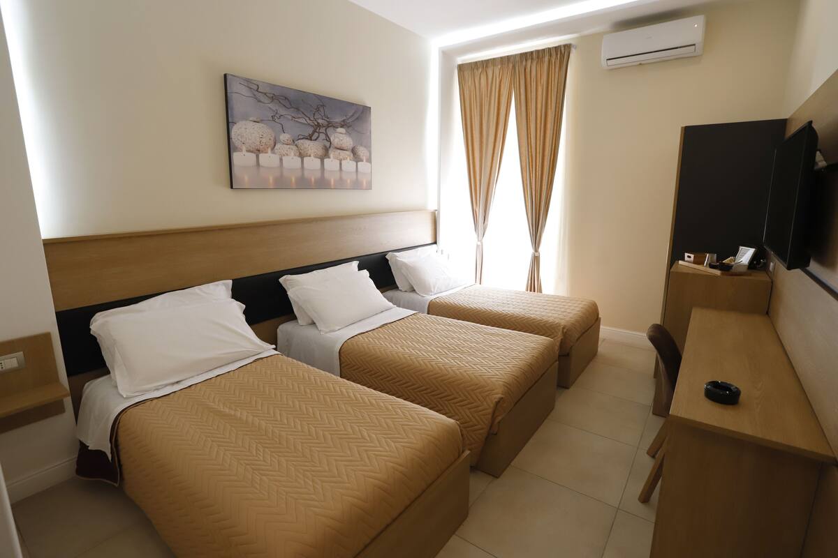 Habitación de hotel con dos camas, un escritorio, una silla, un televisor y un equipo de aire acondicionado.