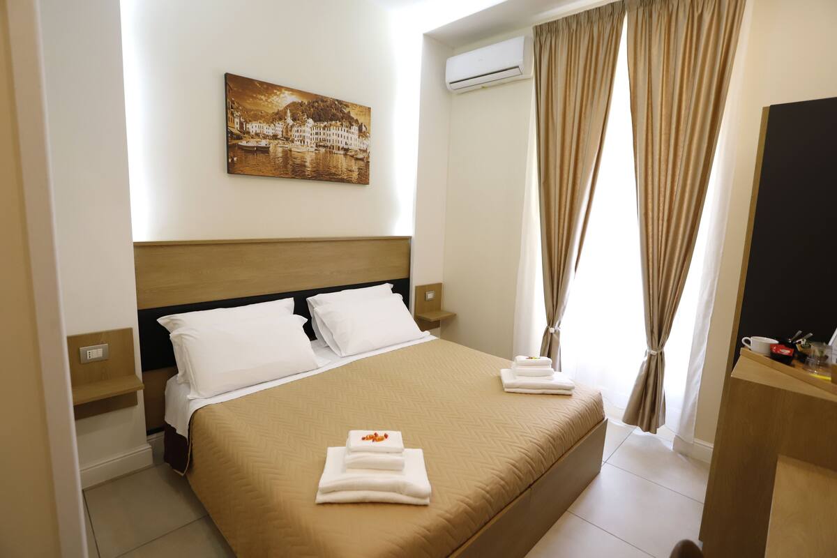 Habitación de hotel con cama, un cuadro, unidad de aire acondicionado y escritorio con espejo.