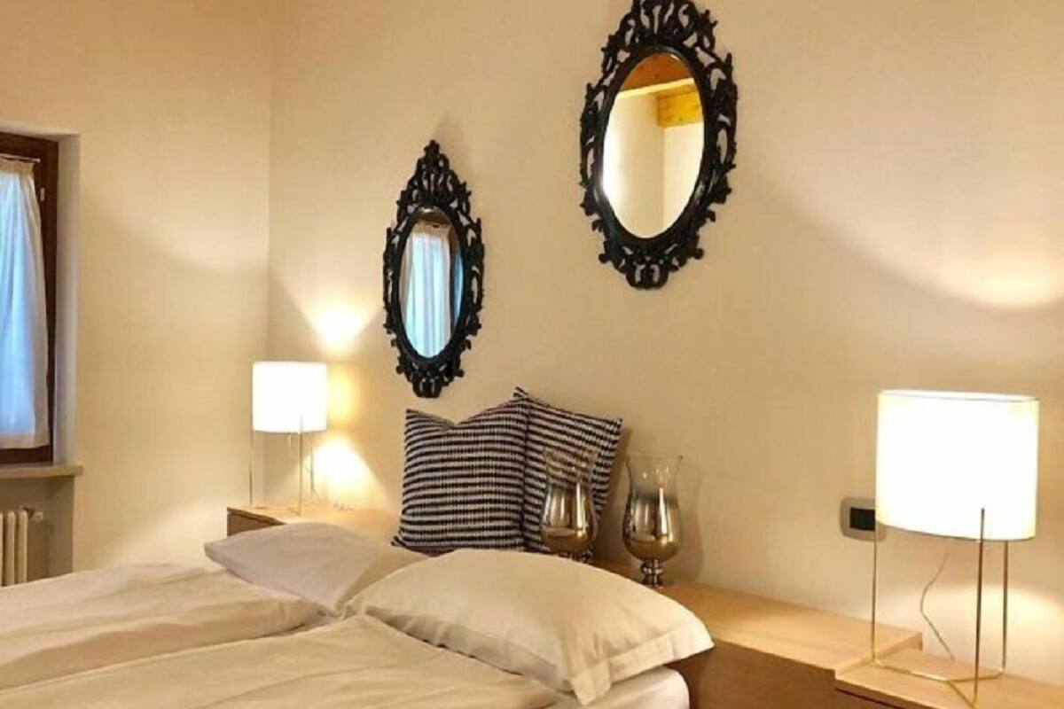 Een hotelkamer met een bed, nachtlampjes, een dressoir en twee spiegels aan de muur.