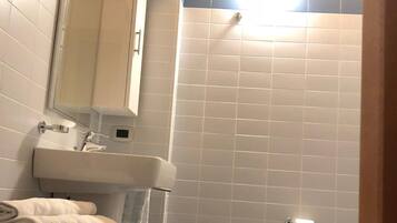 A bathroom with a sink, mirror, towel rack, and a shower area.