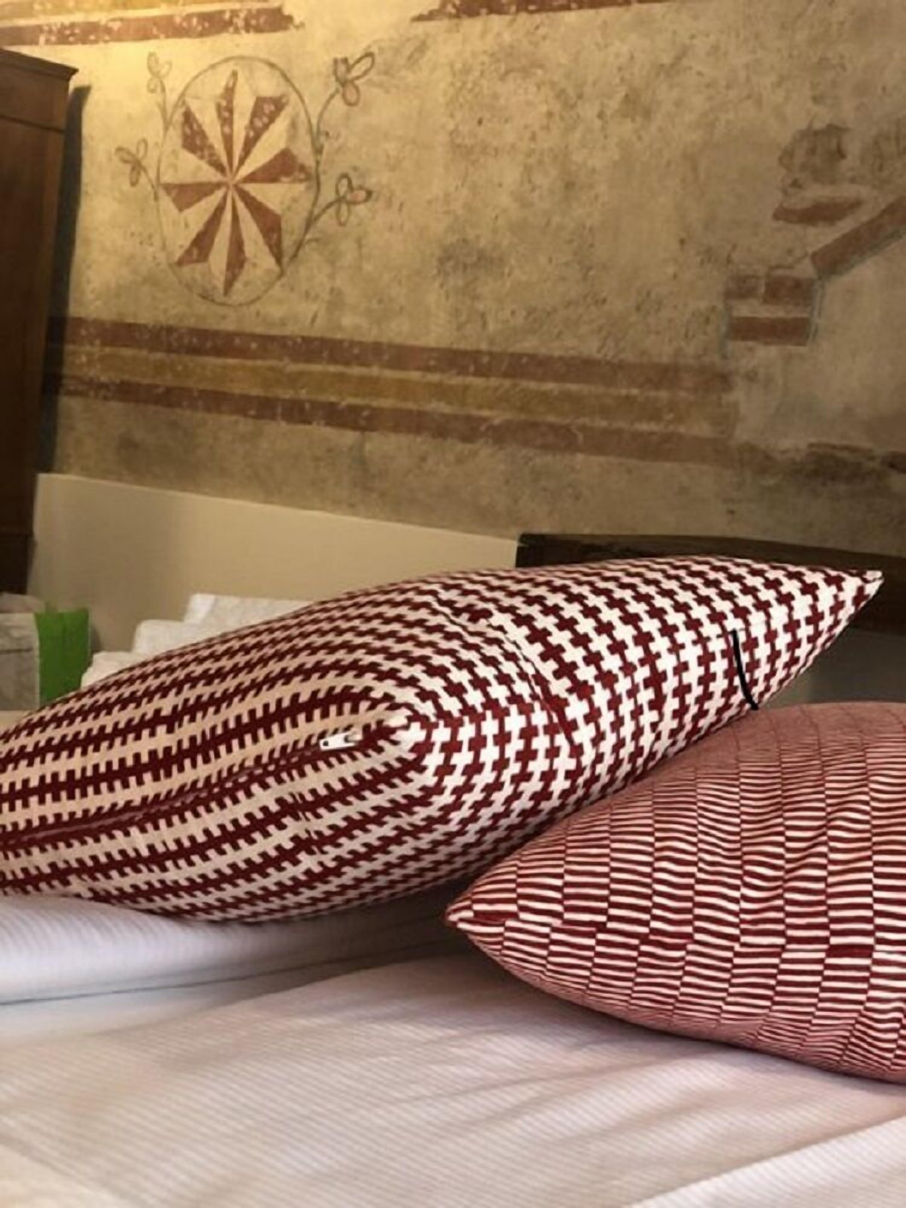 Een bed met twee kussens met een patroon, en een muur met een rond ontwerp en baksteenmotief.