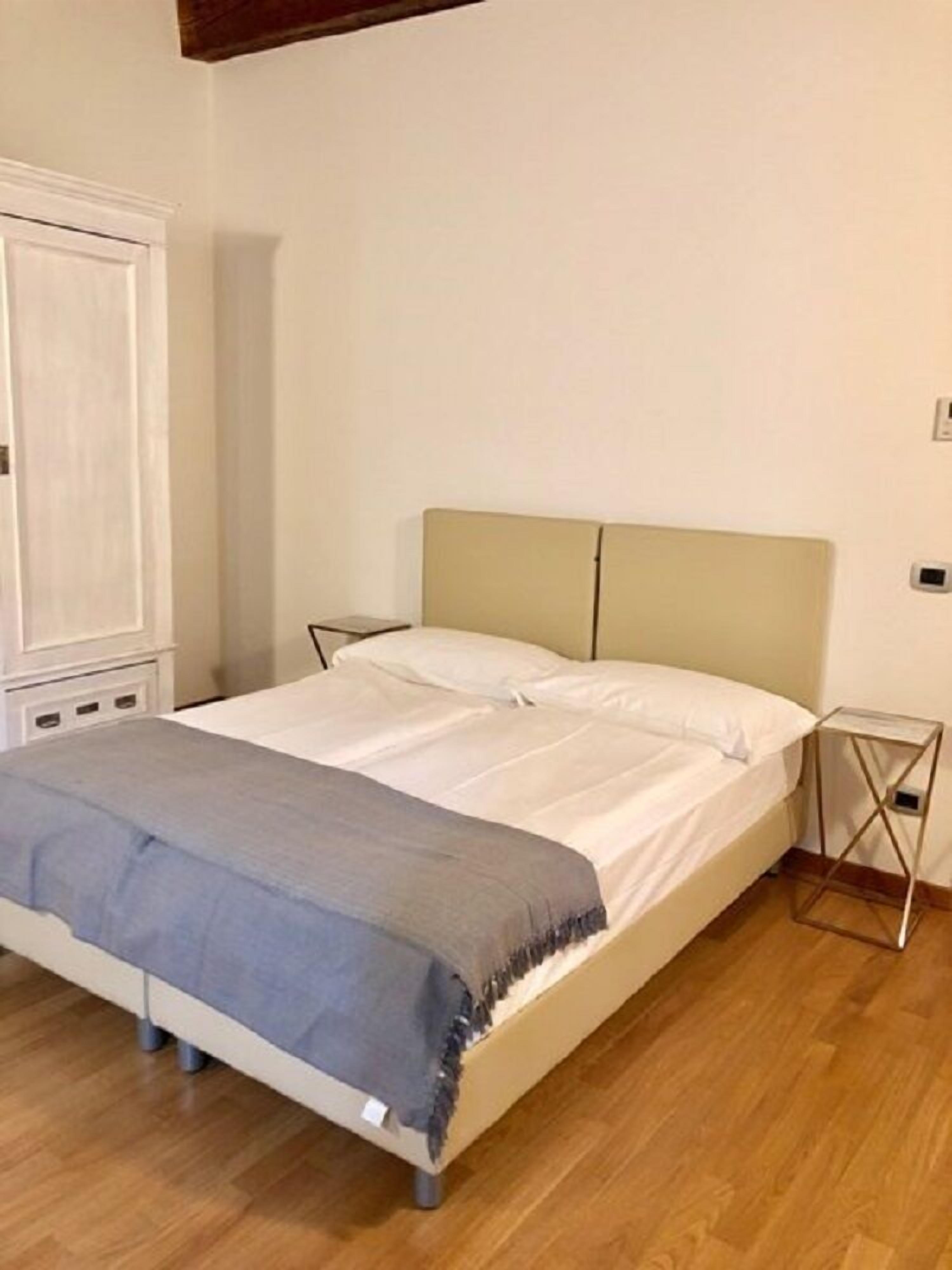 Een eenpersoonskamer met houten vloer, een witte inbouwkast en nachtkastje met lamp.