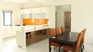 A modern kitchen with white cabinets, an orange backsplash, and a dining area with a black table and brown chairs. - Setia Walk by SYNC (Puchong)