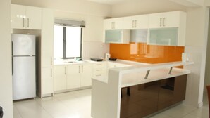 A modern kitchen with white cabinets, a central island, and a window. - Setia Walk by SYNC (Puchong)