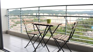 A balcony with a table and chairs, offering a view of a cityscape and hills. - Setia Walk by SYNC (Puchong)