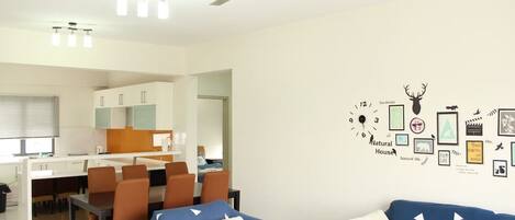 A modern living room with a ceiling fan, a dining area with a white table and brown chairs, and a wall decorated with various framed pictures and a clock.