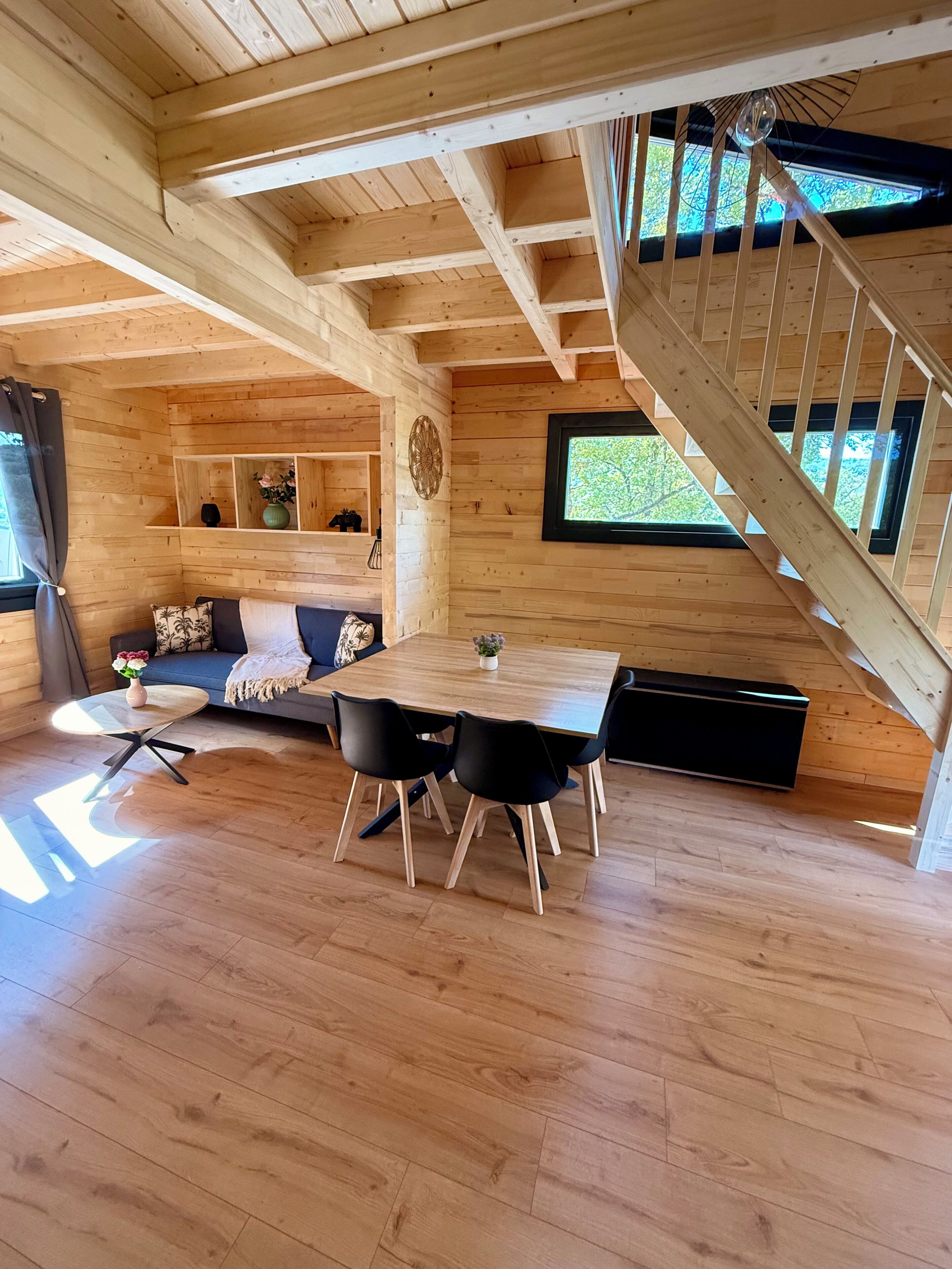 Un interior de fusta amb zona de menjador, sofà i escala.