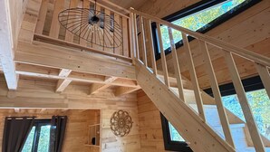A wooden cabin interior with a loft bedroom, a dining area, and a staircase. - Cabanes et Lodges du Belvedere (Serrières-sur-Ain)