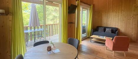 A wooden cabin interior with a round dining table, chairs, a sofa, and a coffee table.
