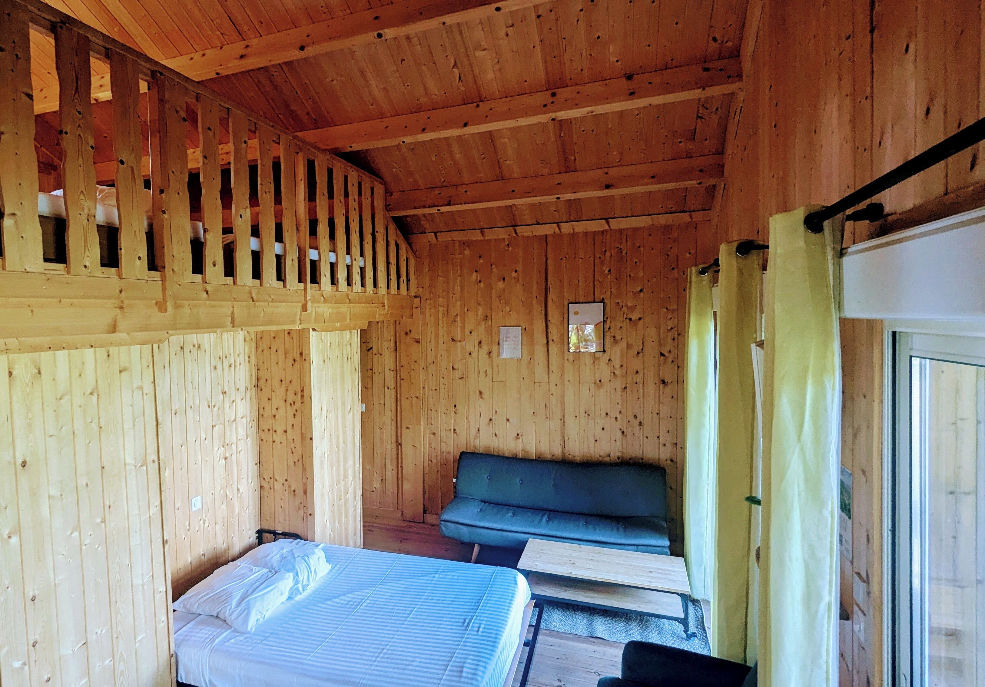 A wooden cabin with a loft bed, a sofa, and a window with curtains.