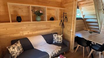 Un interior de cabaña acogedor, con un sofá gris oscuro, una mesa redonda de madera y un comedor con sillas negras.