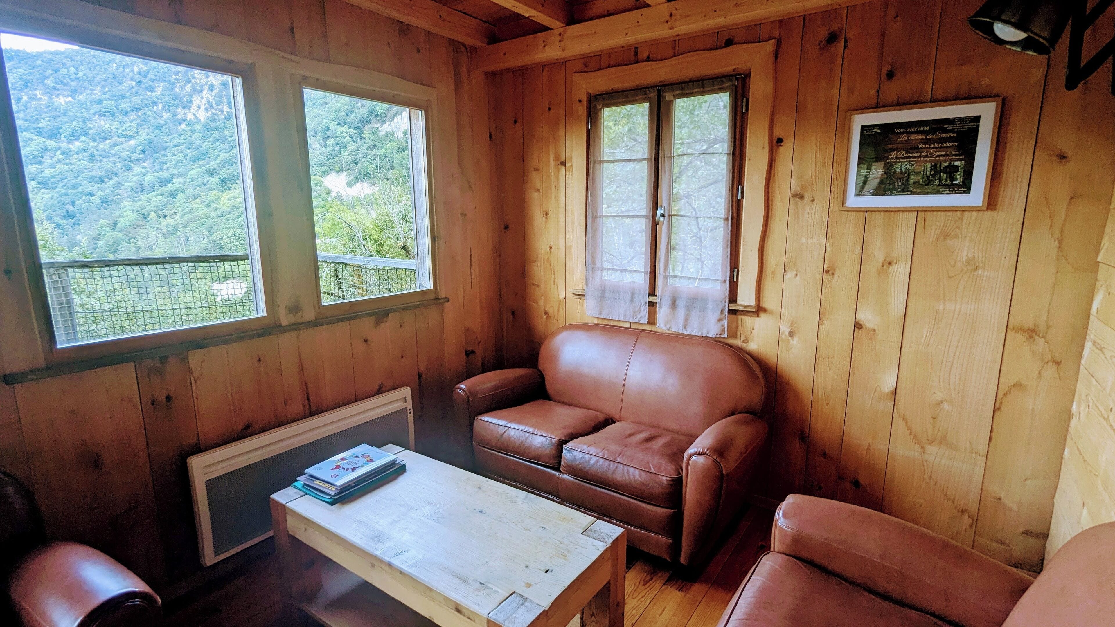 A wooden cabin interior with a brown leather sofa, a small table, and a framed picture on the wall.