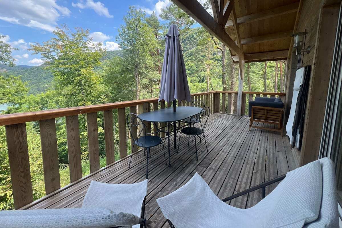 Une terrasse en bois avec une table et des chaises, un banc et une vue sur un paysage boisé.