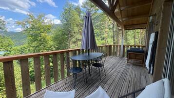 A wooden deck with a table and chairs, a bench, and a view of a forested landscape.