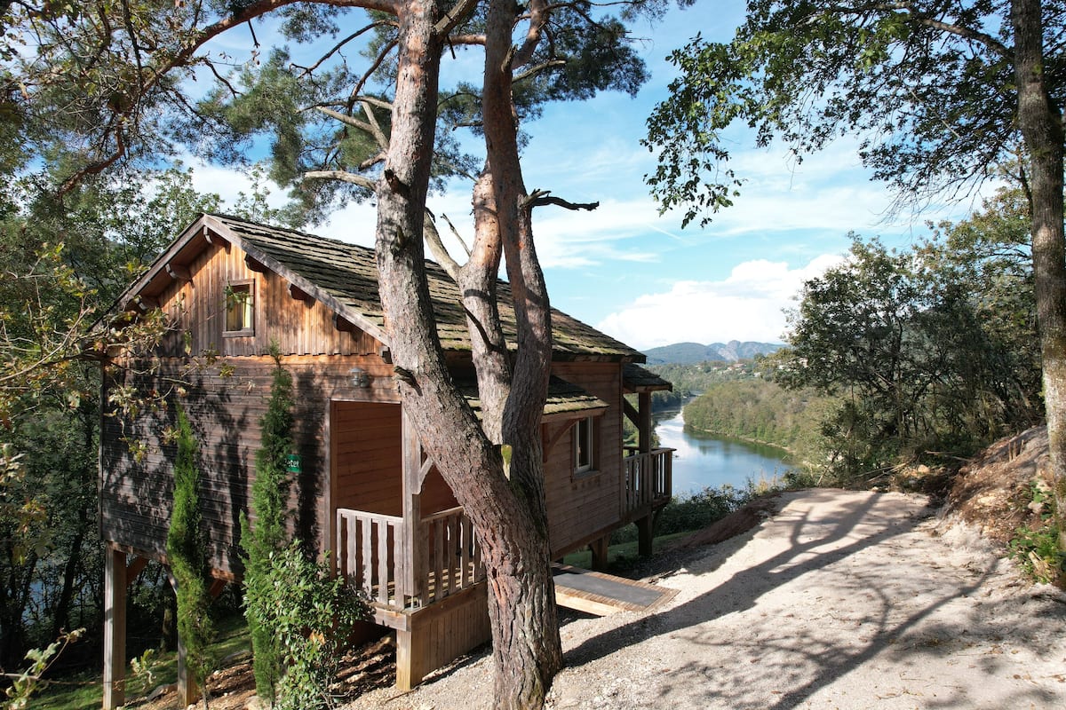 Une cabane en bois dotée d’un balcon, entourée d’arbres et offrant une vue sur un lac.