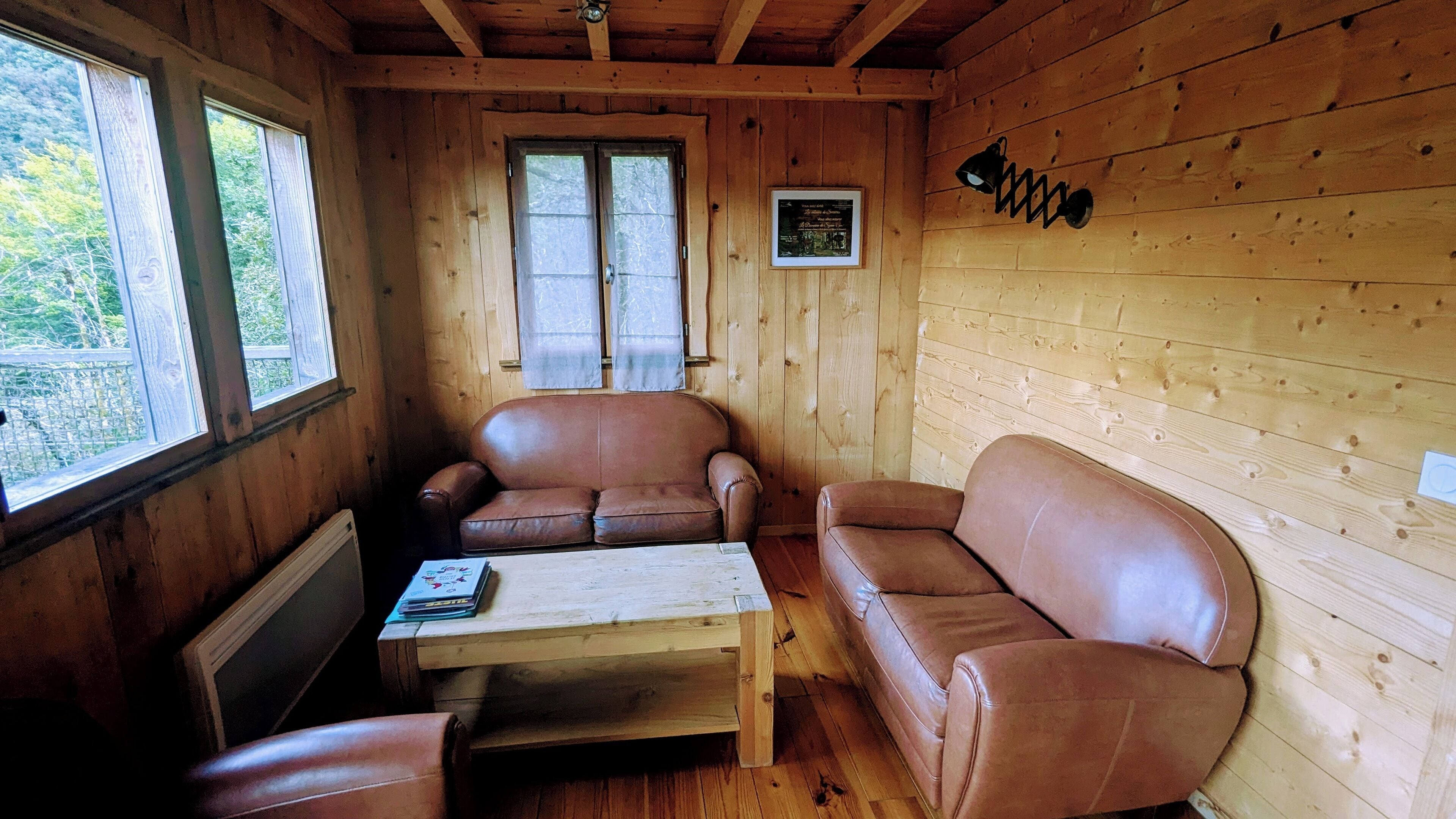 A wooden cabin interior with two leather sofas, a small table, and a framed picture on the wall.