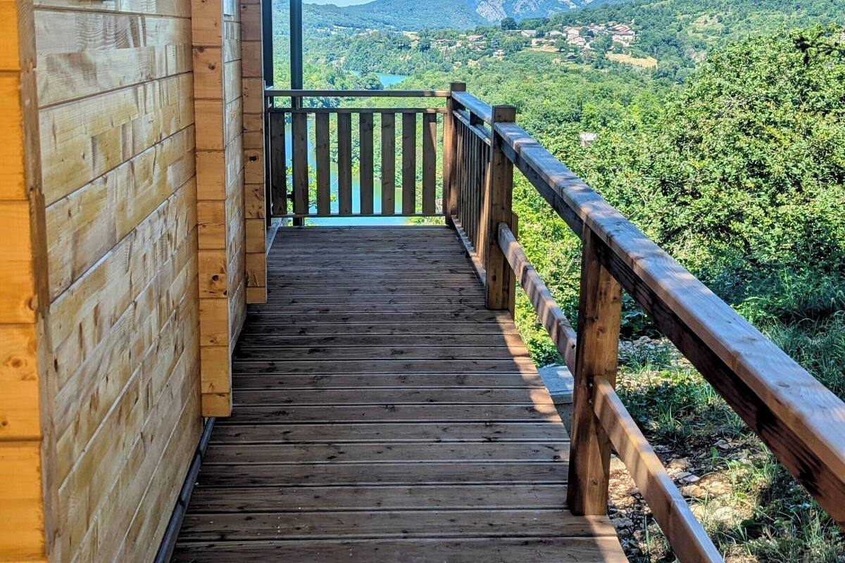 Une terrasse en bois qui mène à un balcon offrant une vue sur un paysage montagneux.