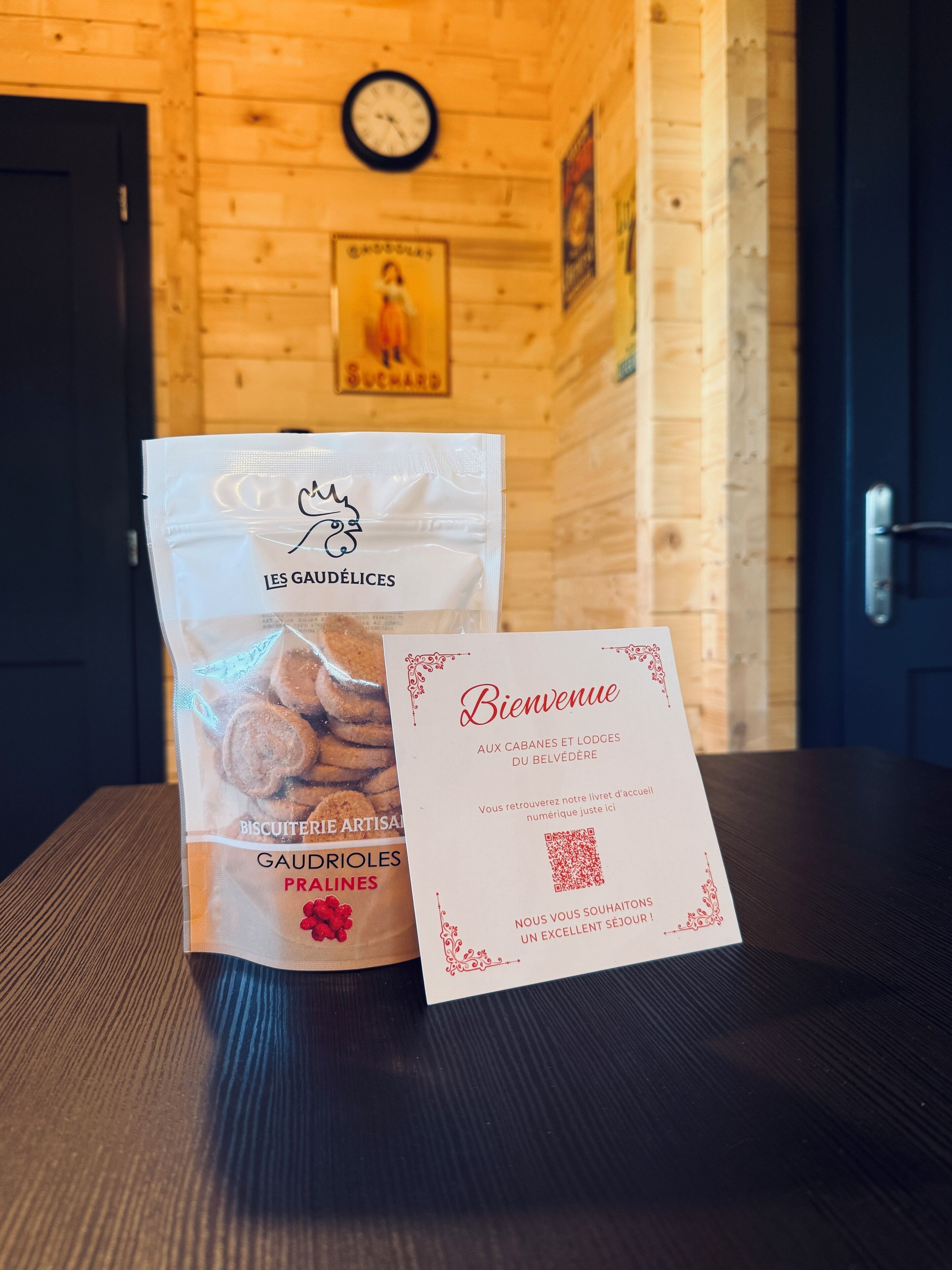 Un intérieur en bois avec une horloge au mur, une porte et une table sur laquelle se trouvent un paquet de biscuits et une carte de bienvenue.