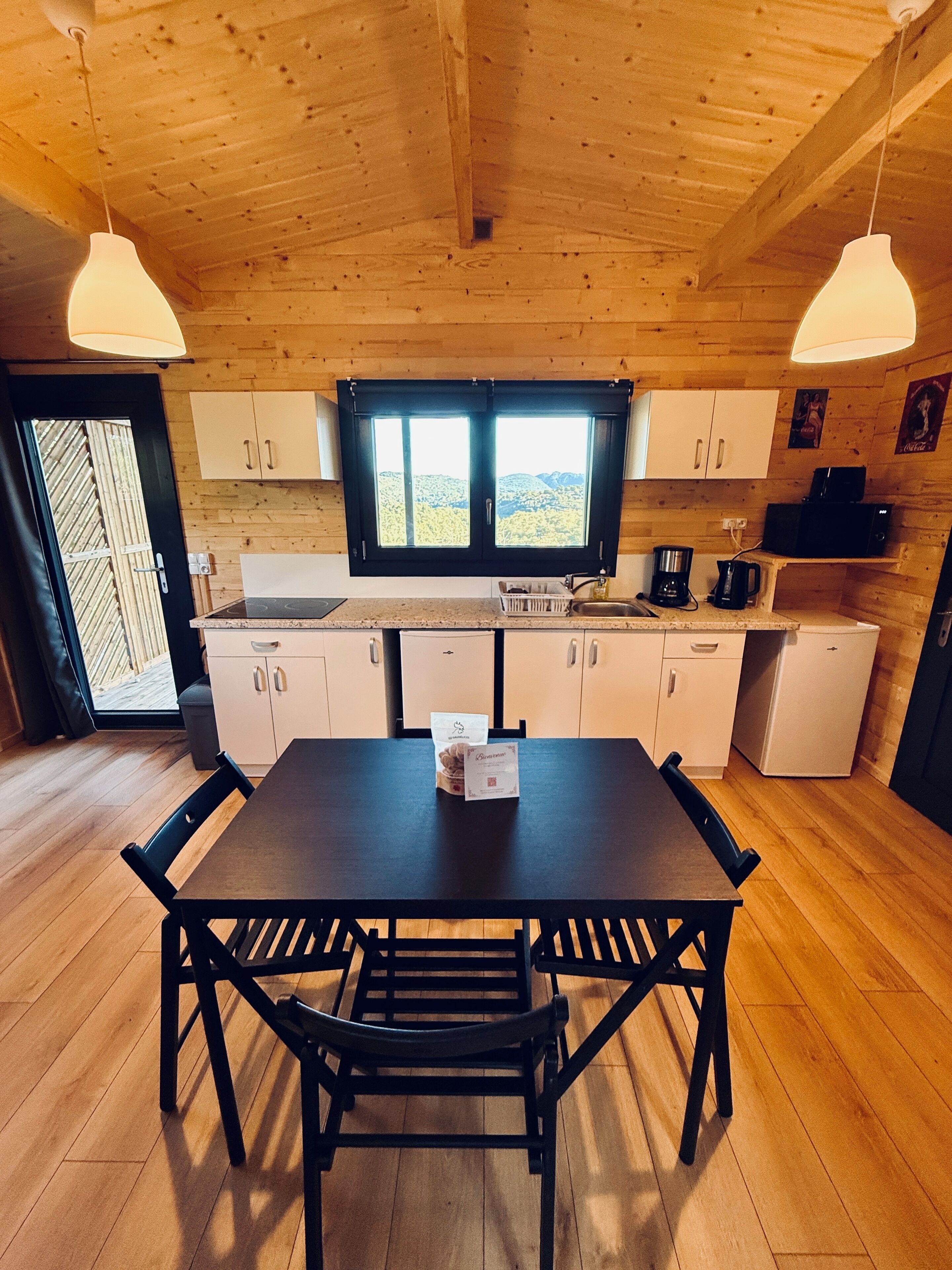 Een houten interieur met een eettafel, stoelen, een raam, kasten en een koelkast.