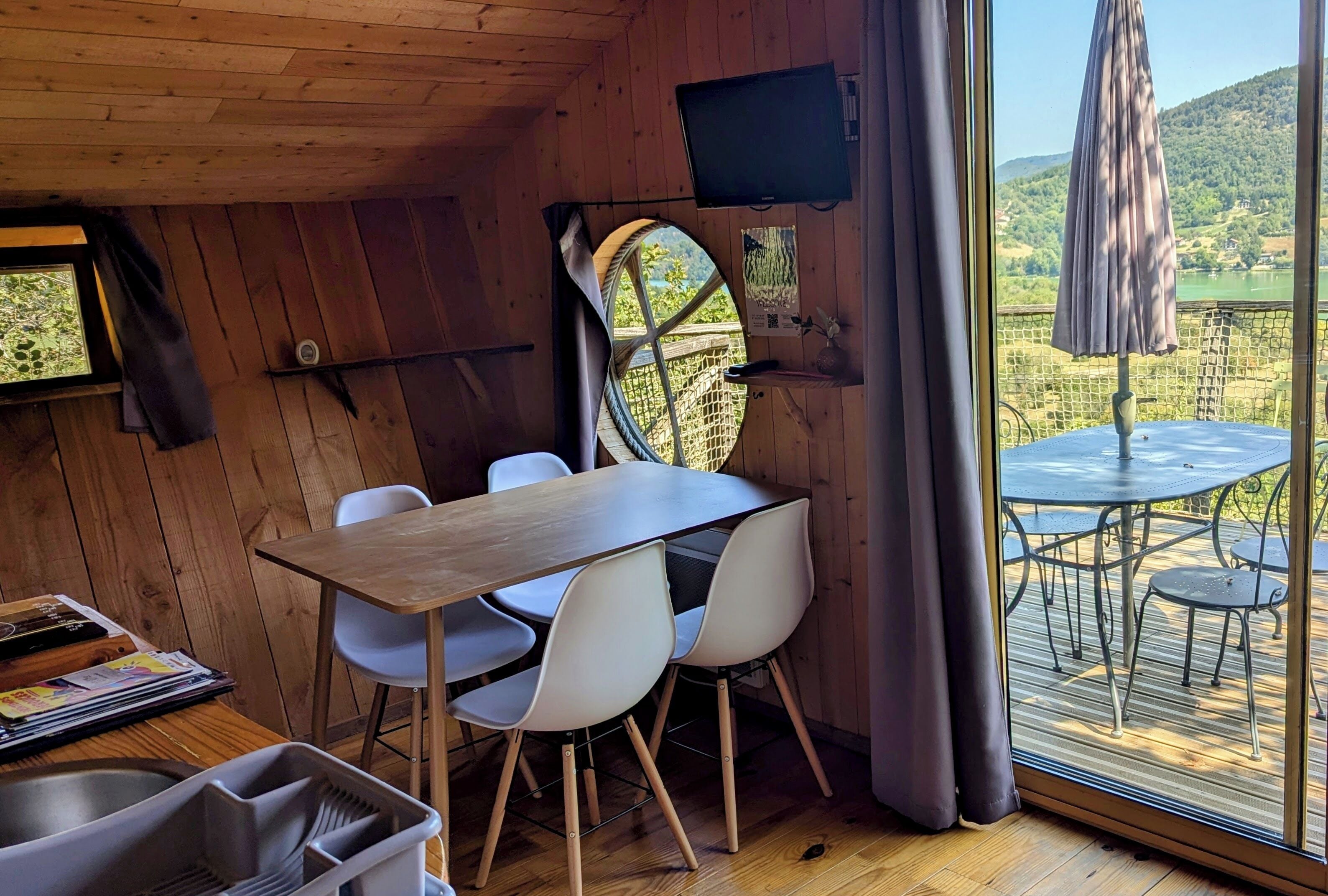 Ein Holzinterieur mit Esstisch, Stühlen, einem Fernseher und Blick ins Freie.
