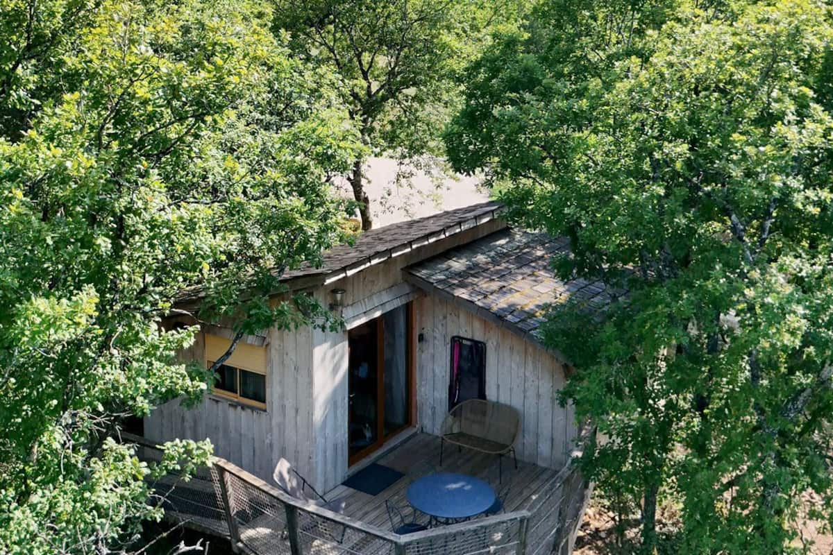 Une cabane en bois dotée d’un balcon, entourée d’une végétation luxuriante.