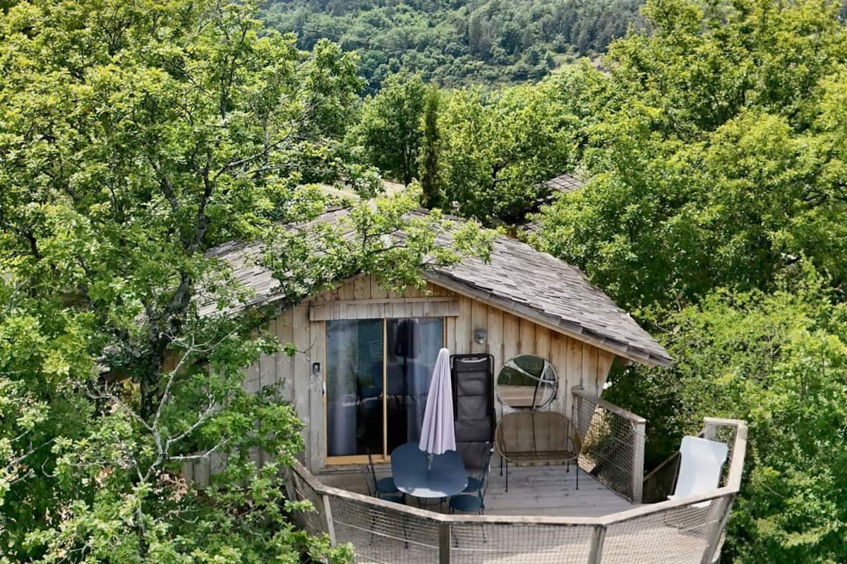 Une cabane en bois dotée d’une terrasse, entourée d’une forêt dense et de collines.