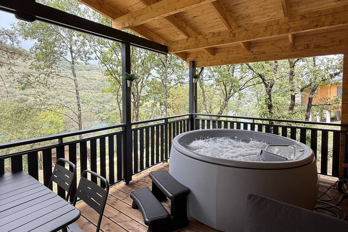 Une terrasse en bois avec un jacuzzi, une table et des chaises.