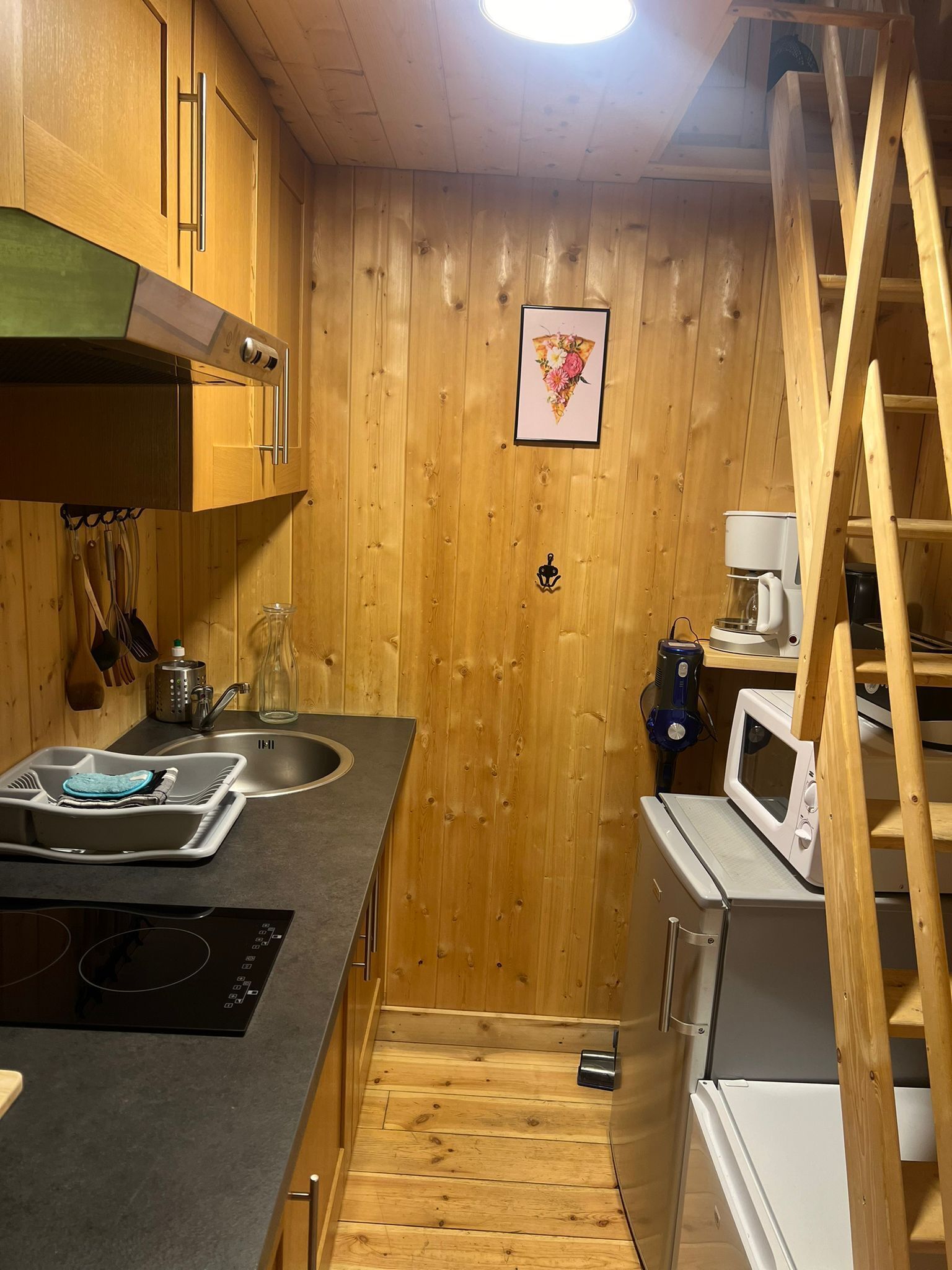 A compact kitchen with wooden walls, a built-in microwave, and a coffee maker.