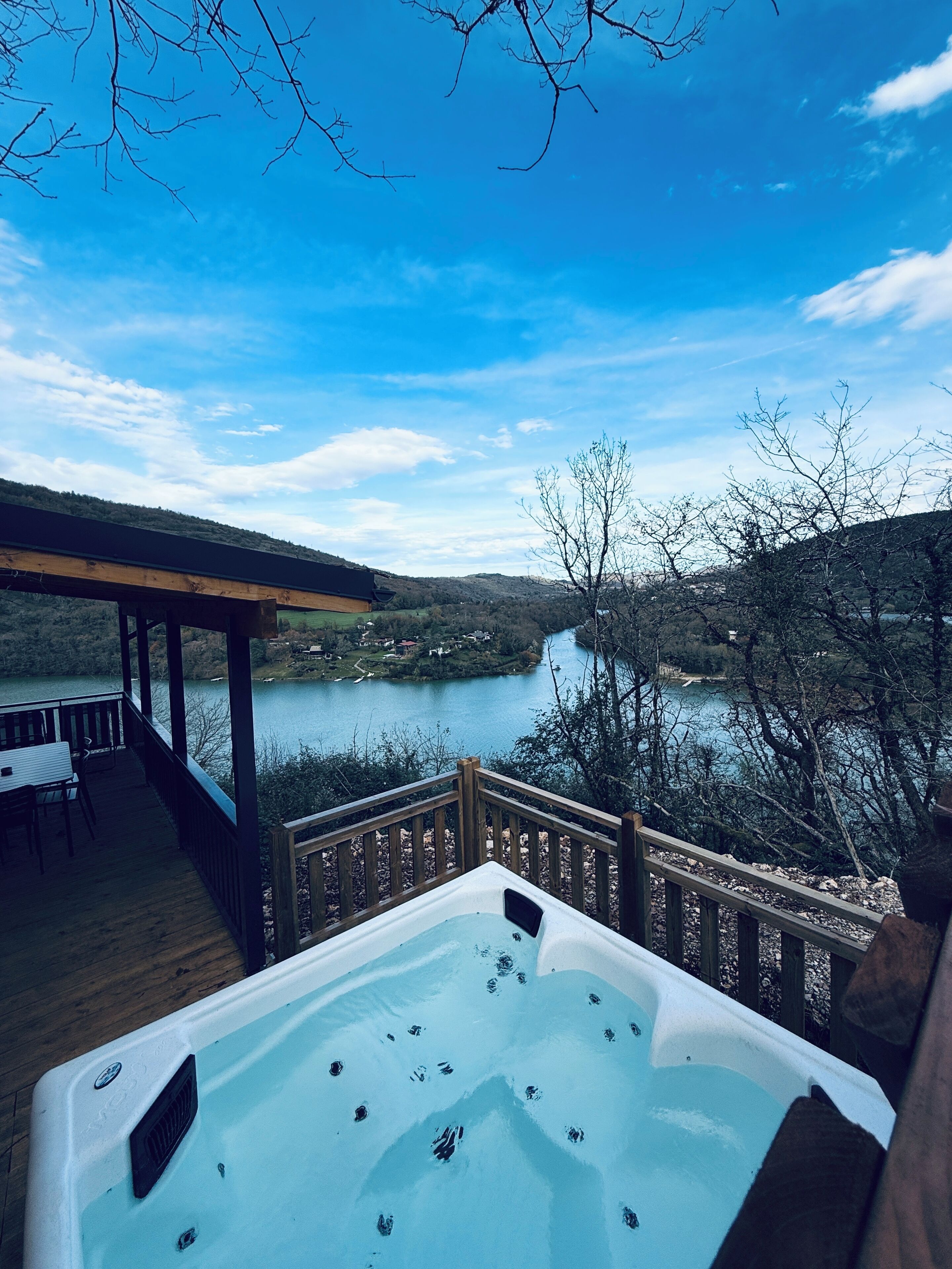 A hot tub on a deck with a view of a lake and hills.