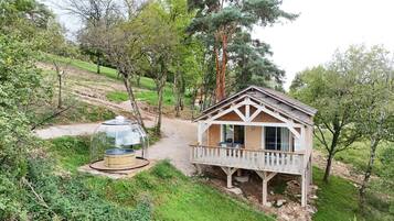A wooden cabin with a balcony, surrounded by trees and a clear path.