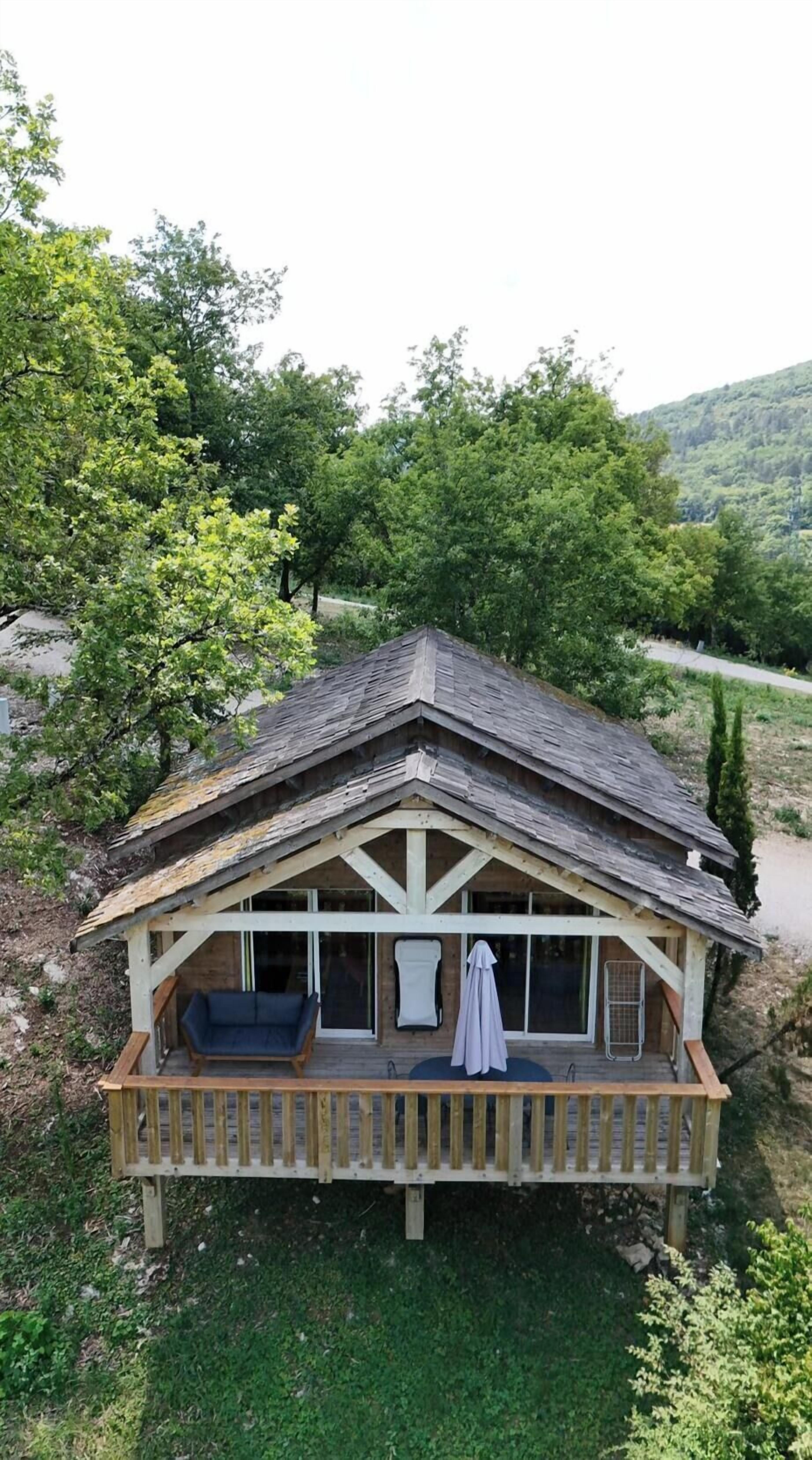 A wooden cabin with a balcony, surrounded by greenery and hills.