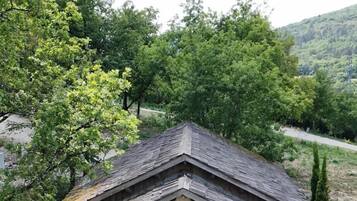 A wooden cabin with a balcony, surrounded by greenery and hills.