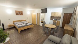 Habitación compacta con cama, una pequeña mesa de comedor con sillas, un sofá, televisión y kitchenette.
