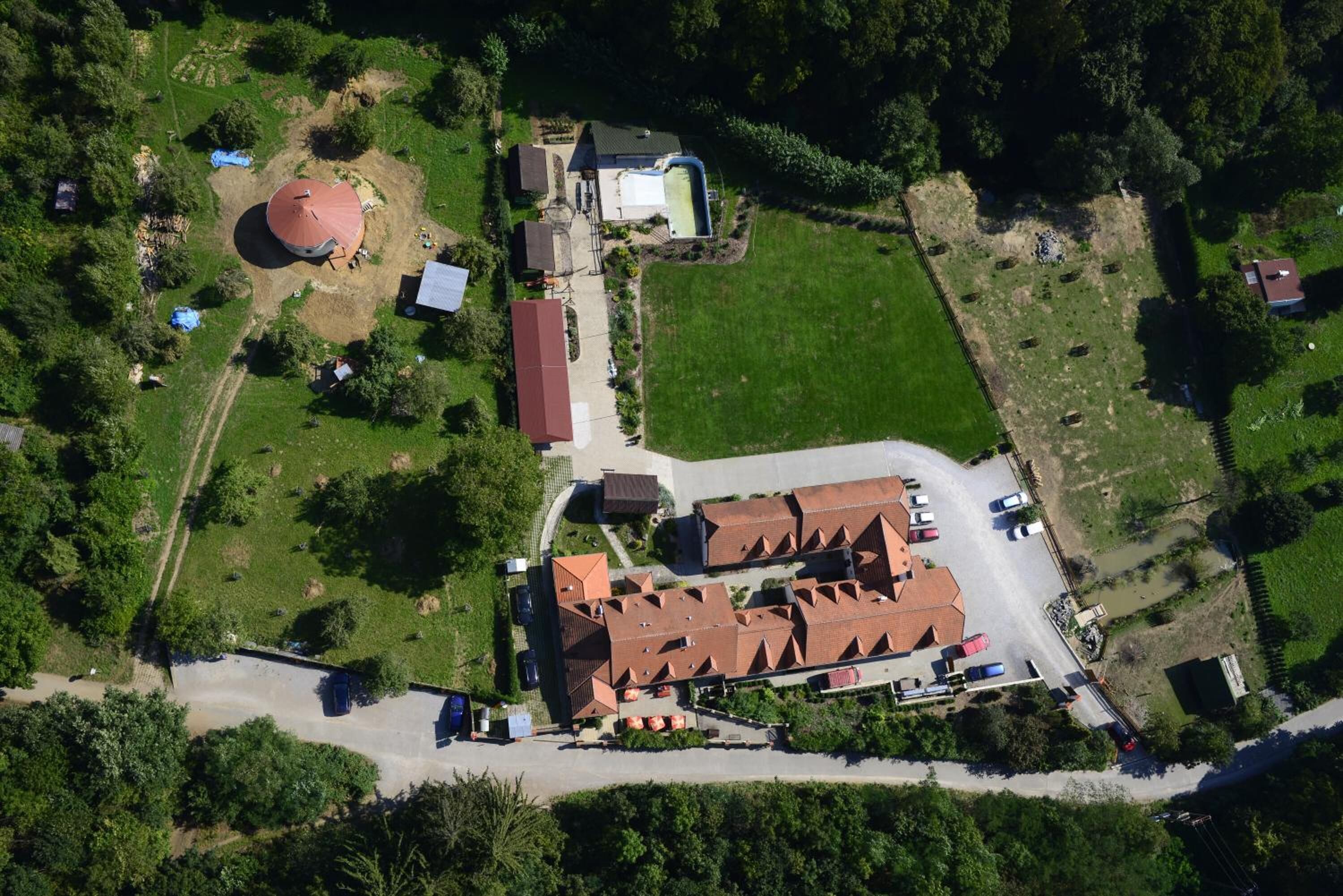 Vista aérea de una propiedad con un edificio grande de techo rojo, una piscina y una estructura circular.