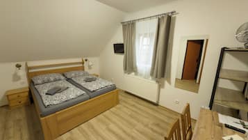 A bedroom with a wooden bed, a desk with a chair, a radiator, and a window with curtains.