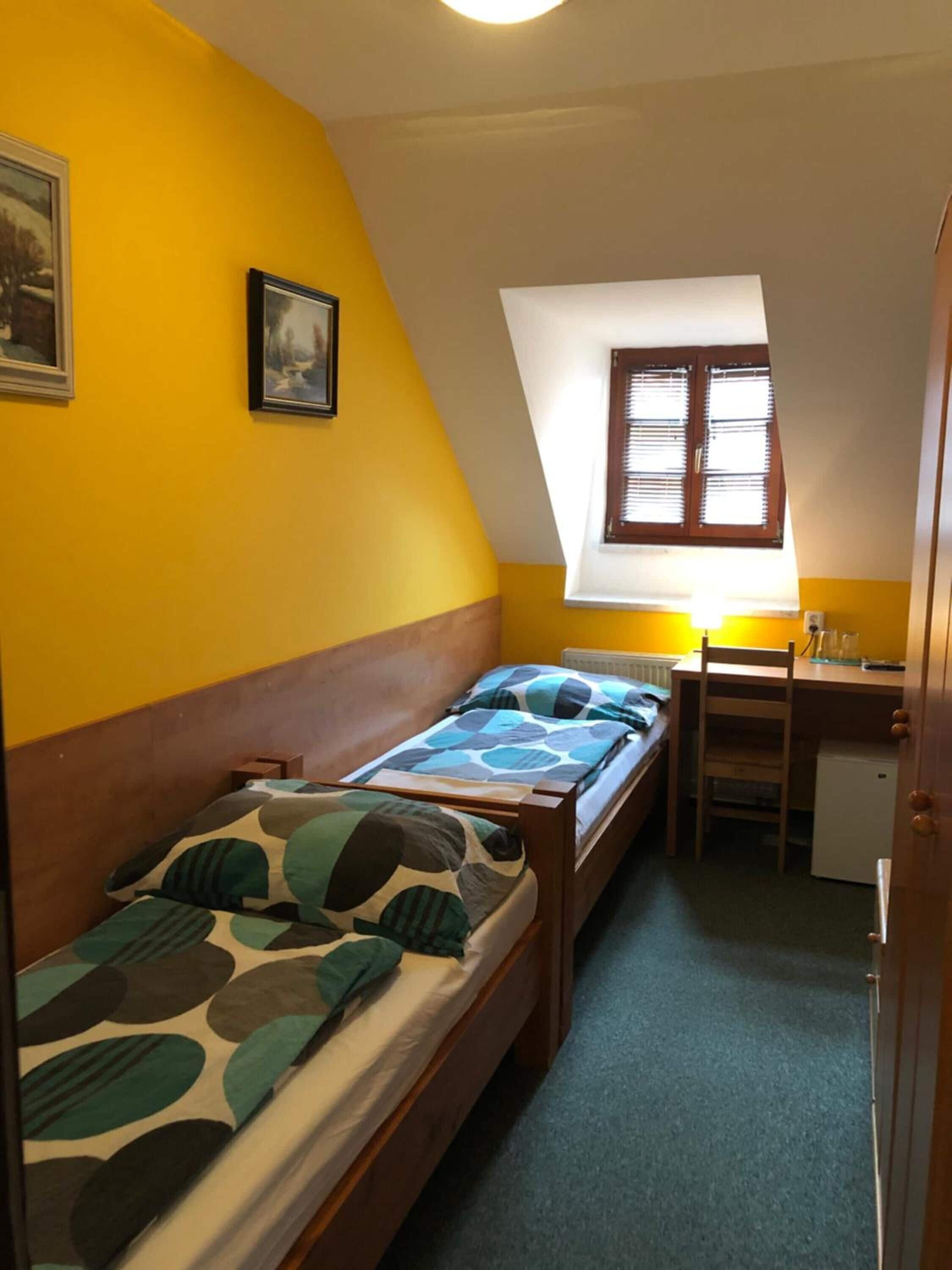 Una habitación pequeña y acogedora con dos camas individuales, un escritorio y una ventana.