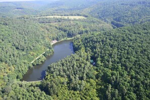 Une vue aérienne d’une zone boisée, avec une rivière, un petit bâtiment situé près de la rivière et un bâtiment plus grand, visible au loin.