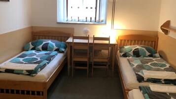 Quarto pequeno e acolhedor com duas camas de solteiro, uma escrivaninha de madeira e uma janela com persianas.